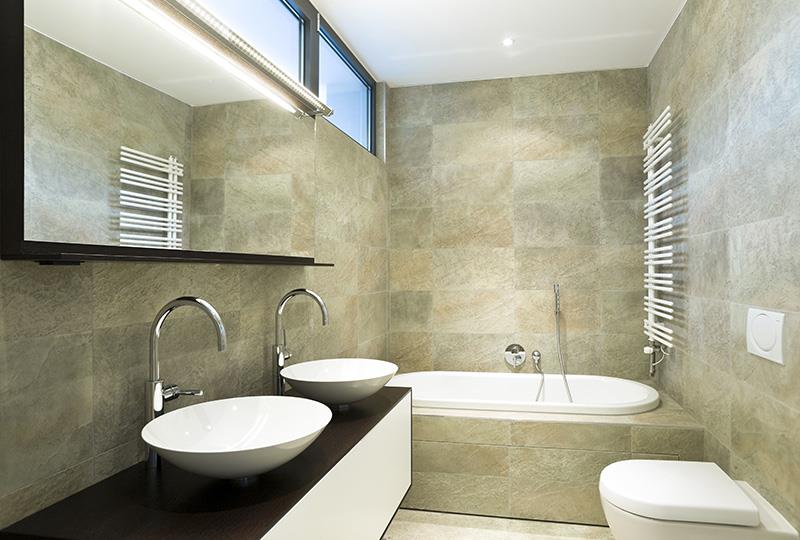 Salle de bain tendance chic avec carrelage aux murs, baignoire encastrée, WC et vasques posées sur un meuble suspendu. 