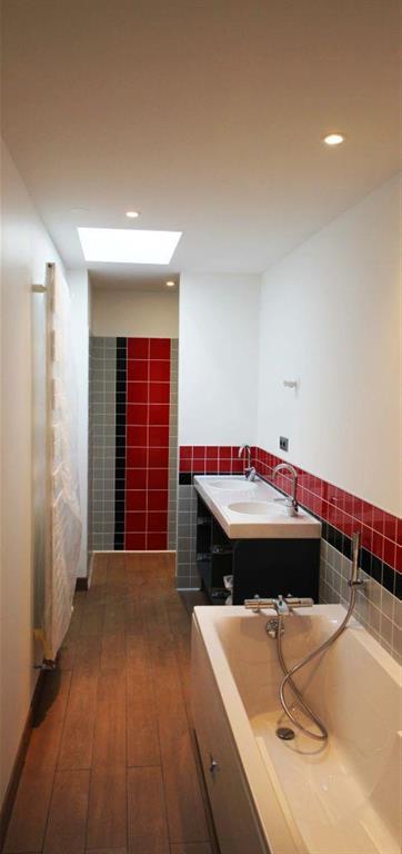 Salle de bain contemporaine avec baignoire. Carrelages rouges, gris et noirs. Parquet, murs blancs 