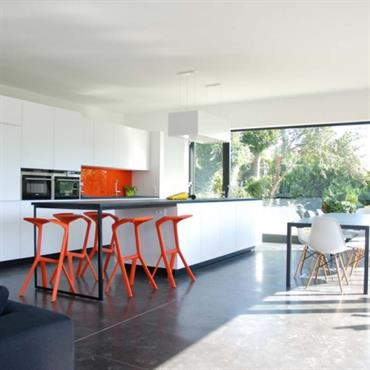 Grande cuisine ouverte sur la pièce à vivre. L'utilisation de la couleur orange relève les blanc et gris foncé. 