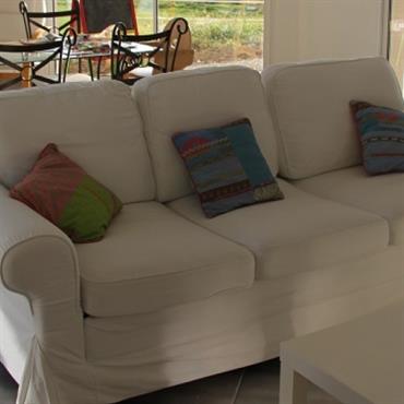 Salon avec canapé blanc et salle à manger, avec plateau en verre et chaises en fer forgé 