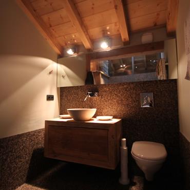 Salle de bain avec WC, mosaïque grise, meuble suspendu en bois, poutres apparentes. 