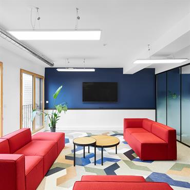 Salle de réunion cosy avec canapés rouges Salle de réunion cosy avec canapés rouges, tables gigognes et écran mural, bibliothèque noire, moquette à dessins géométriques