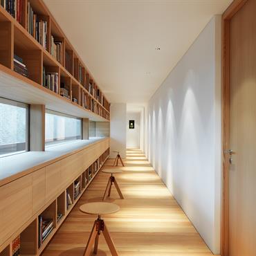Couloir aménagée en longue bibliothèque. Cadrage sur le paysage par des fenêtres en bandeau. 