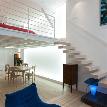 Le mur de lumière souligne la hauteur du loft dont les deux niveaux sont reliés par  l'escalier suspendu en chêne blanchi. 