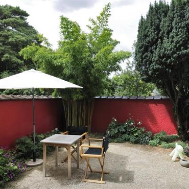 Mur de la terrasse peint en rouge, en contraste avec le vert des la végétation. 
