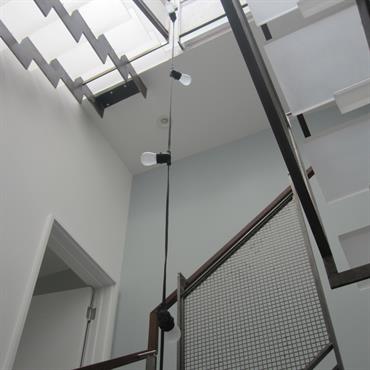 Escalier contemporain transparent. Limon central en acier. Garde corps en acier et main courante en bois. Puits de lumière avec guirlande d'ampoules 
