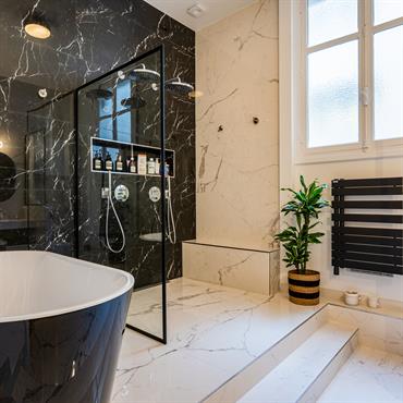 Aménagement d'une grande salle de bain en marbre noir et blanc comportant une double douche et une baignoire ilot.Petit détail de l'architevte, on doit monter 2 marches pour y accéder 