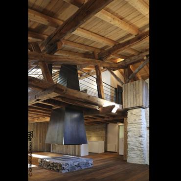 Pièce principale avec cheminée centrale finition acier noir, sole foyère en pierres de pays, habillage vieux bois, aciers doux 