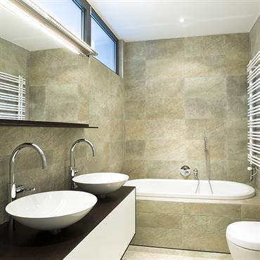 Salle de bain tendance chic avec carrelage aux murs, baignoire encastrée, WC et vasques posées sur un meuble suspendu. 