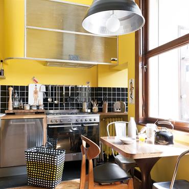 Cuisine moderne aux murs jaunes. Crédence en carrelages noir brillant. Parquet et mobilier en bois 