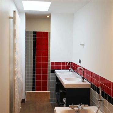 Salle de bain contemporaine avec baignoire. Carrelages rouges, gris et noirs. Parquet, murs blancs 
